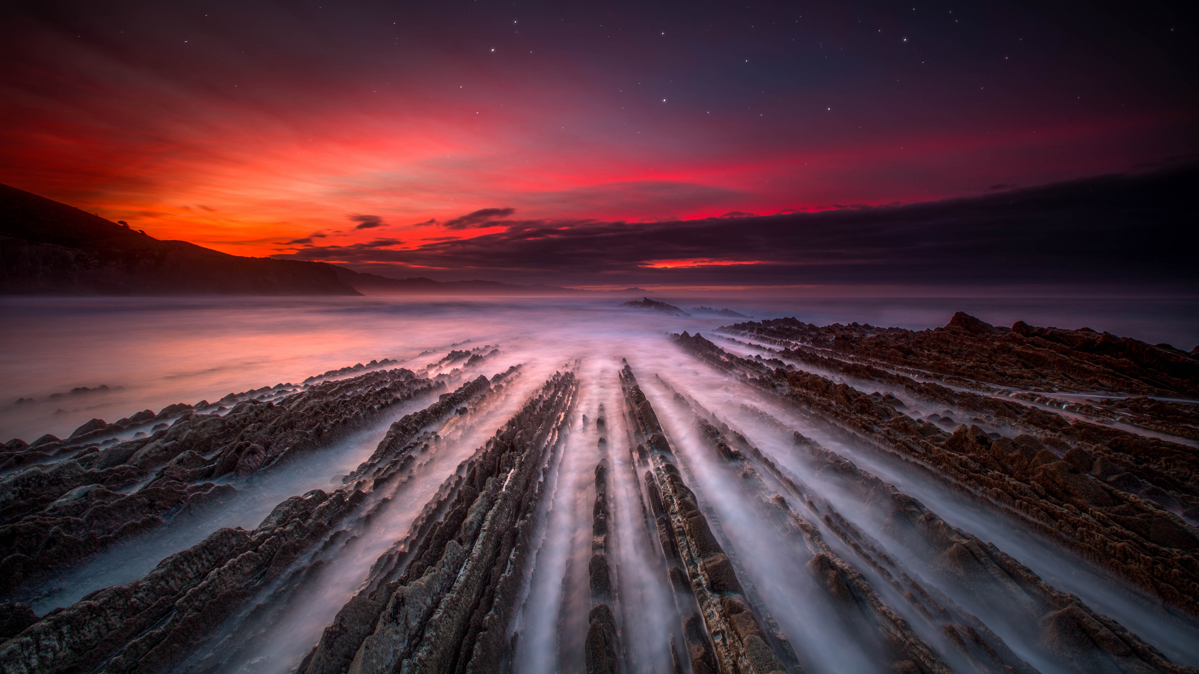 This stunning 4K wallpaper showcases the magnificent Flysch Formation in Zumaia, a beautiful coastal town in the Basque Country. The rugged rock formations contrast beautifully with the sea and the surrounding landscape, making this a perfect wallpaper for nature and outdoor enthusiasts.