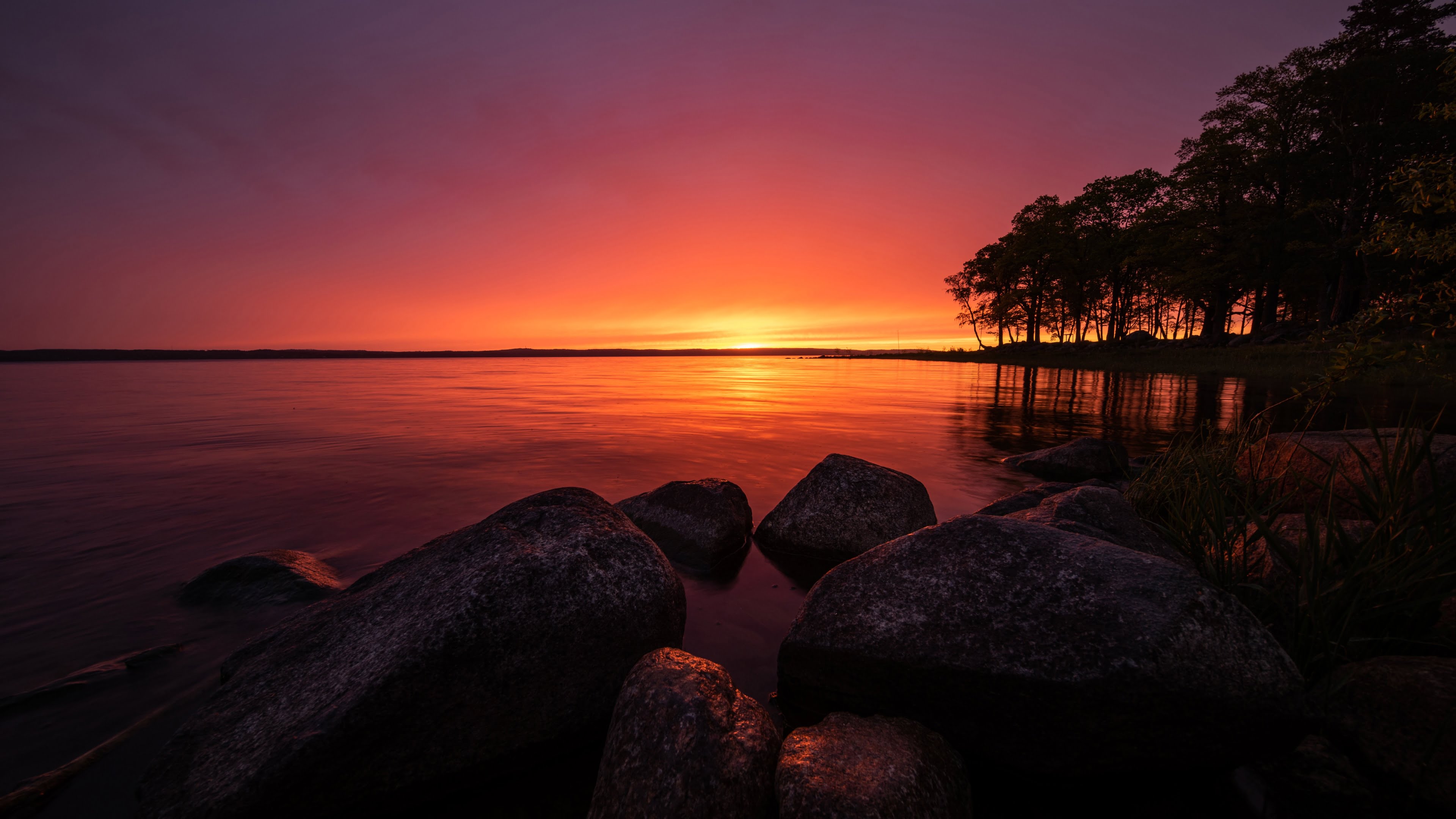 Witness the breathtaking beauty of a sunrise over Roxen Lake in Sweden with this stunning 4K wallpaper. The tranquil lake, surrounded by the Scandinavian landscape, is bathed in the warm hues of the rising sun, offering a serene and peaceful escape. Ideal for travelers and those seeking a desktop background that captures the natural tranquility and Scandinavian charm of this stunning lake at dawn.