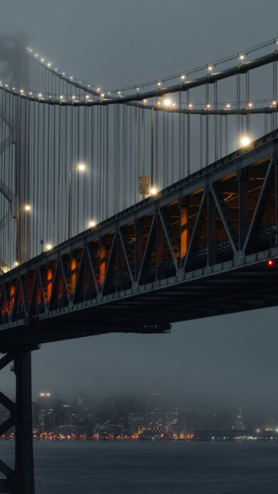 A stunning 4K wallpaper featuring the San Francisco Bay Bridge at dusk. The bridge is beautifully illuminated against a backdrop of the vibrant evening sky, capturing the city's iconic skyline. Ideal for setting as your desktop or mobile wallpaper.